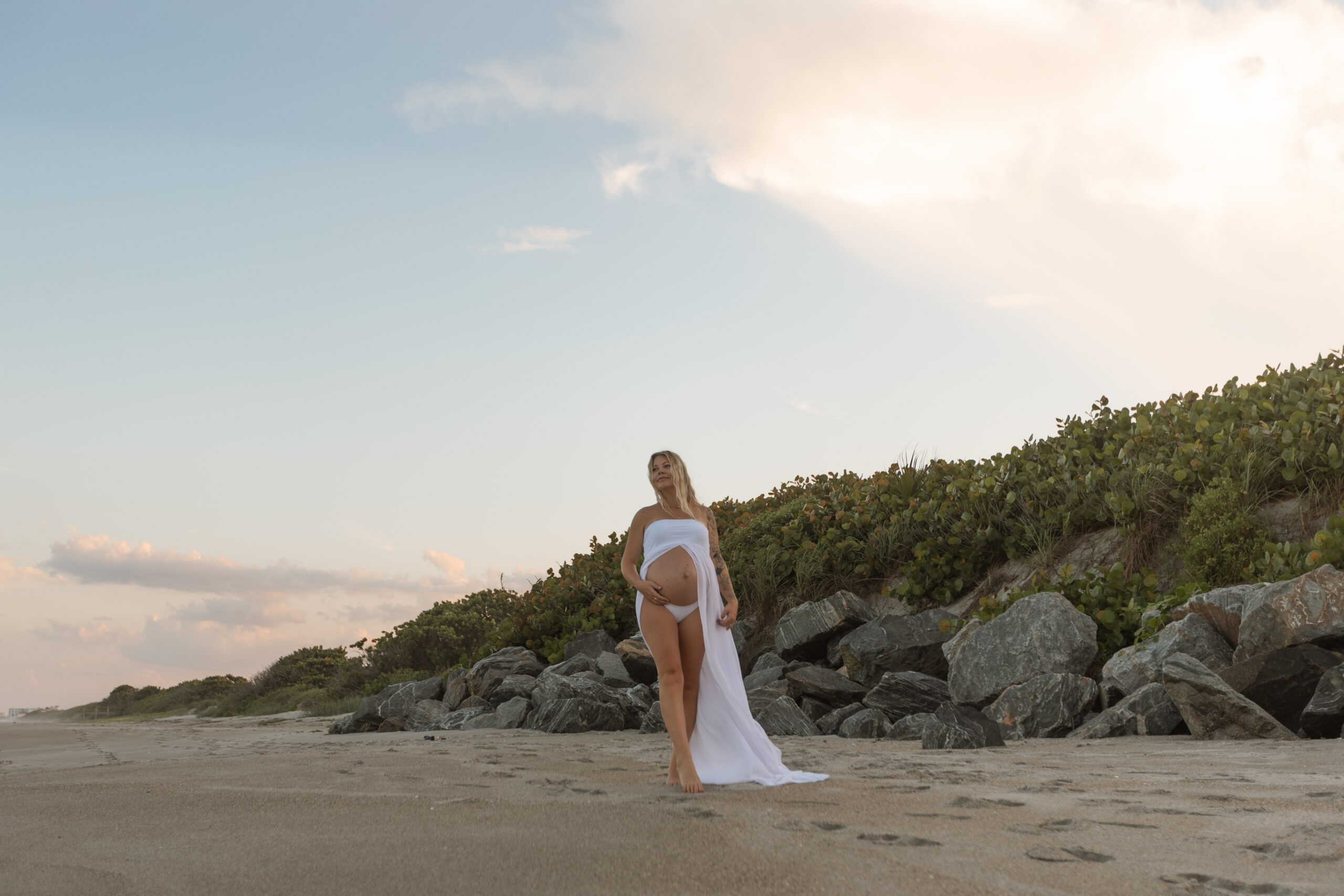 Expecting mother enjoying maternity photoshoot by The Deans Photography during golden hour in Cocoa Beach, Florida.