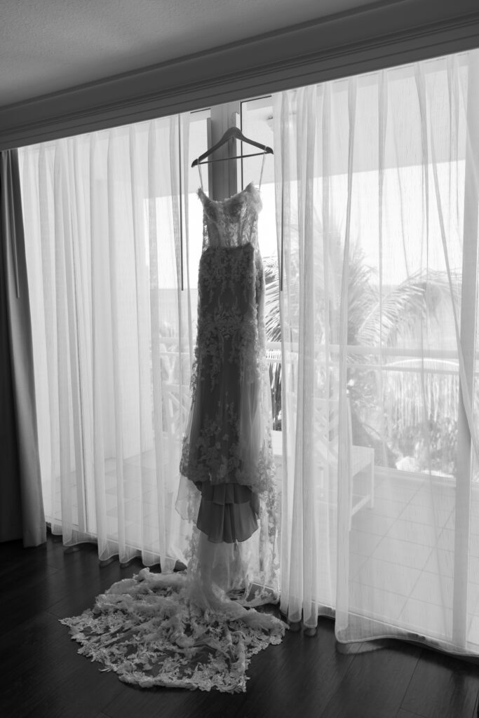 Close-up of the bride's elegant wedding dress hanging on a wooden hanger at The Reefhouse in Key Largo, with soft sunlight filtering through the windows, captured by The Deans Photography