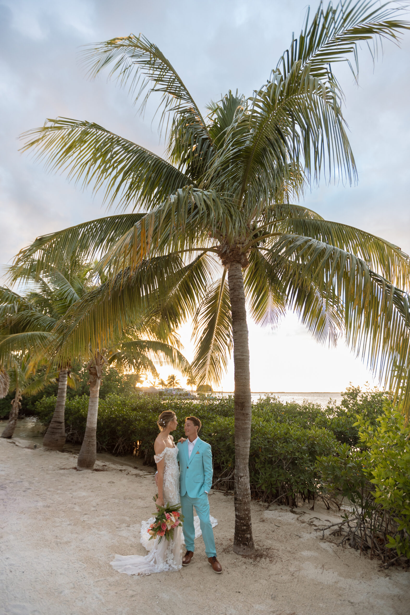 Bride and groom embrace during their wedding photoshoot at The Reefhouse, with lush tropical greenery and the calm waters of the Florida Keys surrounding them.