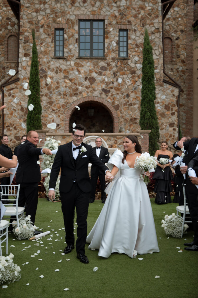 Outdoor wedding ceremony at Bella Collina, photographed by The Deans Photography, with guests in front of the picturesque Tuscan-inspired venue and lush rolling hills.