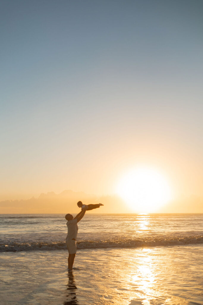 The dad holding his toddler on Cocoa Beach at sunrise, creating memories during a family photography session.