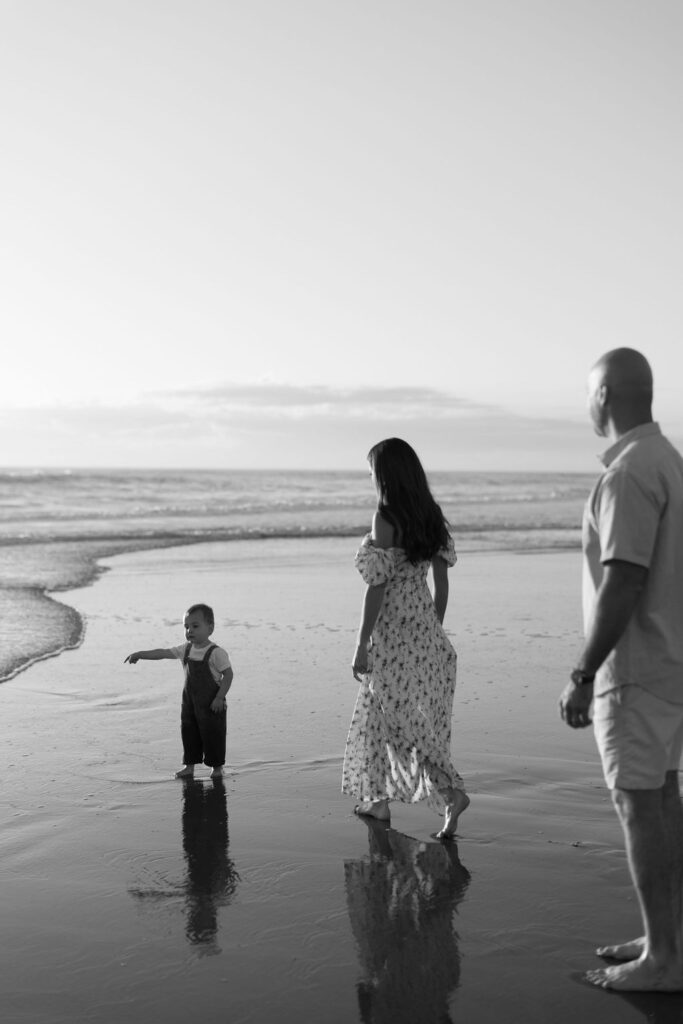 Family of three walking barefoot along the shoreline of Cocoa Beach during sunrise, capturing memories with golden light