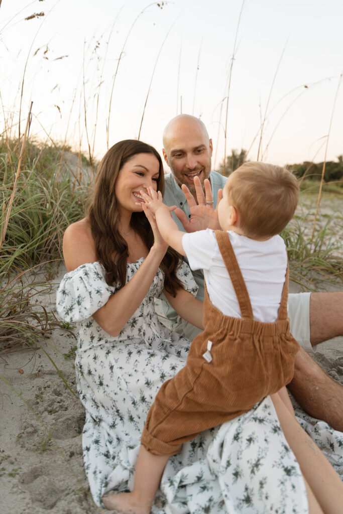 Family of three sitting together on Cocoa Beach during a sunrise photography session, with gentle waves and early morning light.