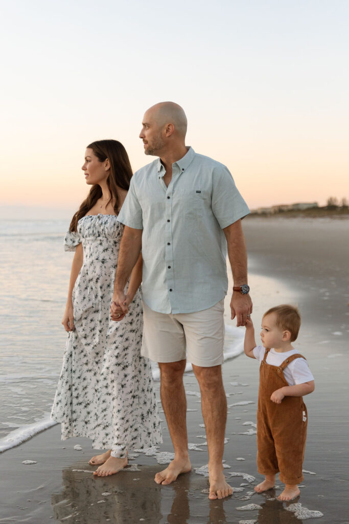 Family of three looking out over the ocean during a family beach session on Cocoa Beach at sunrise