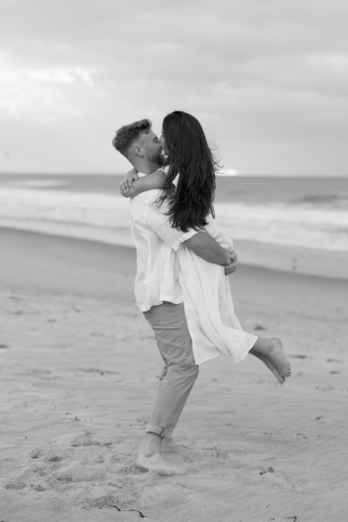 Romantic engagement kiss between couple on Cocoa Beach at sunset, captured by The Deans Photography with a breathtaking backdrop.