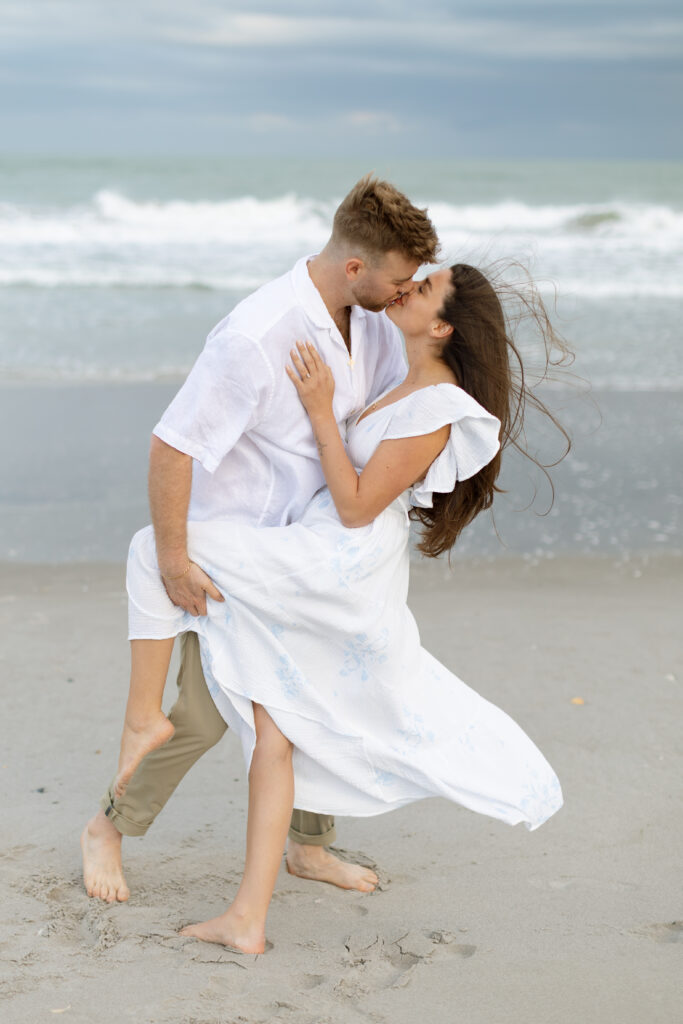 Couple embracing and sharing a romantic kiss in front of the ocean.