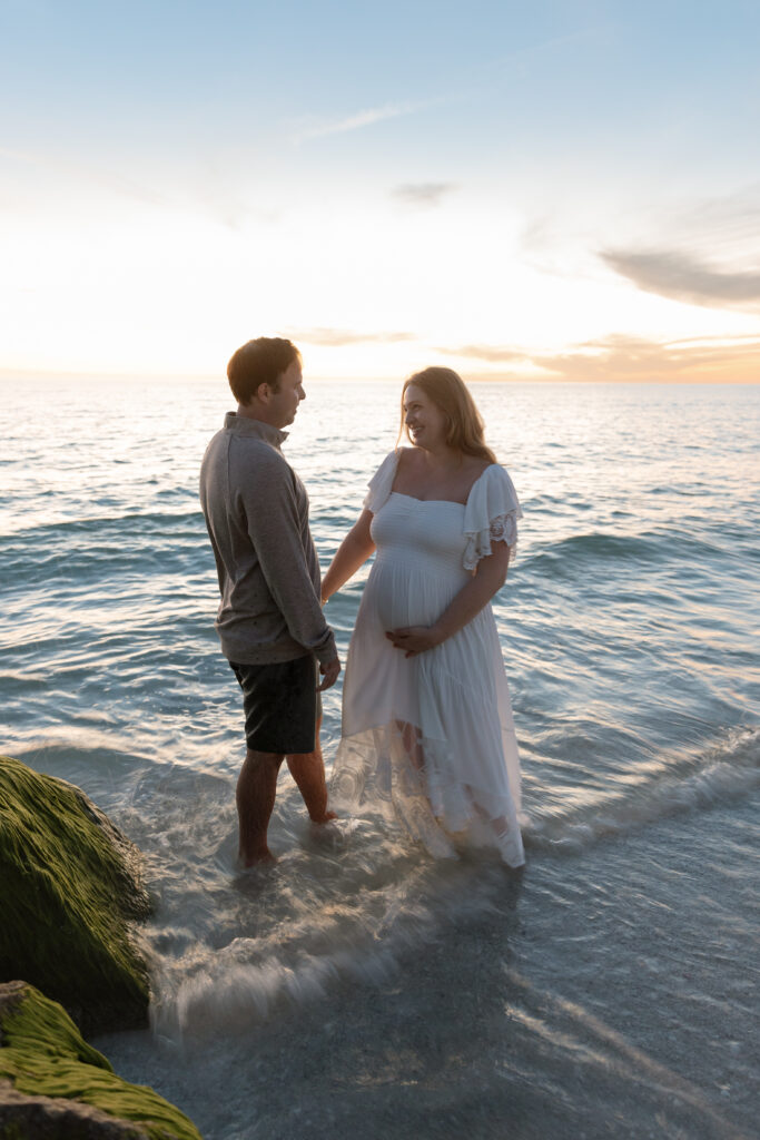 Expecting couple strolling on a Central Florida beach during a maternity photoshoot at sunset.