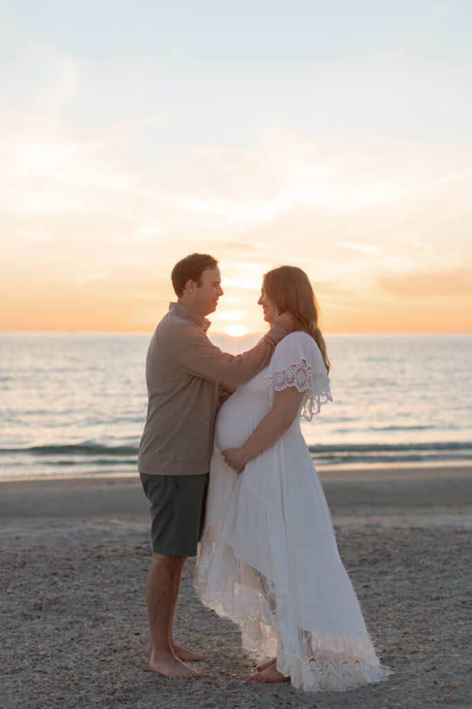 Expecting couple strolling on a Central Florida beach during a maternity photoshoot at sunset.