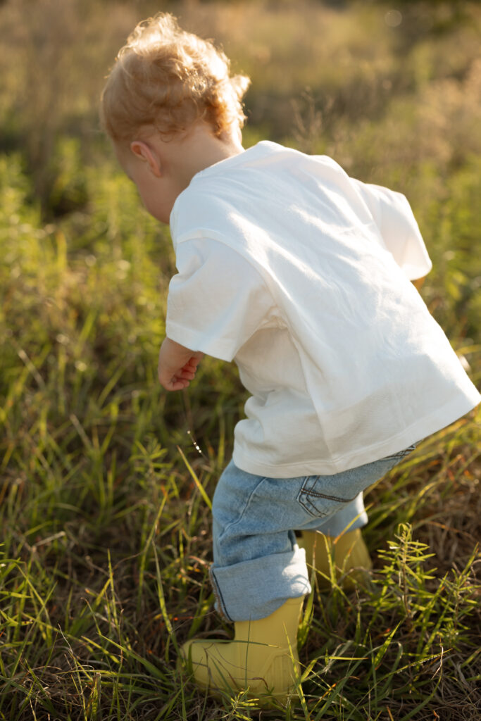 Toddler in white shirt and jeans and yellow rain boots during outdoor motherhood session