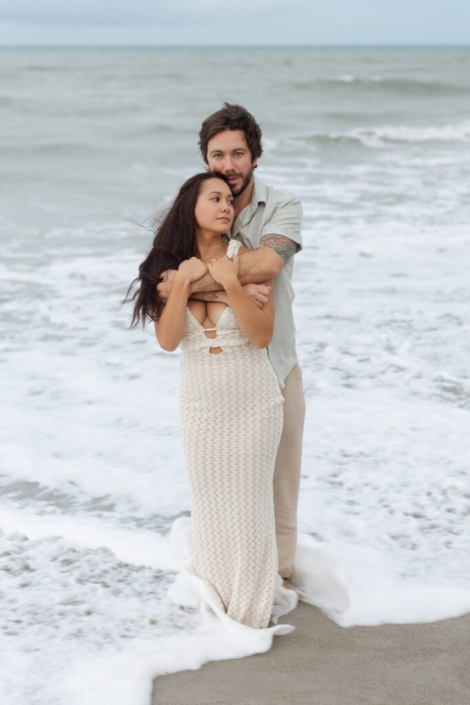 Cocoa Beach, Florida engaged couple wearing soft neutrals sitting on the sand