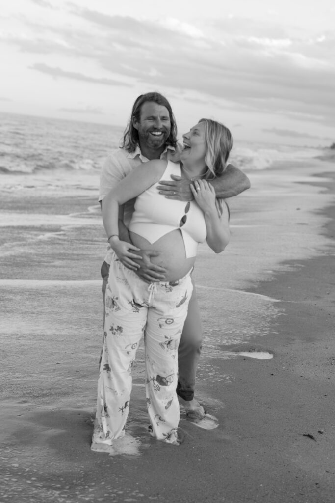 Couple standing along the coastline during their maternity session