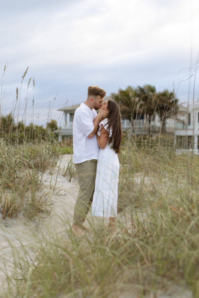 Couple embracing along the shoreline at golden hour, wearing neutral-toned outfits that flow in the breeze.