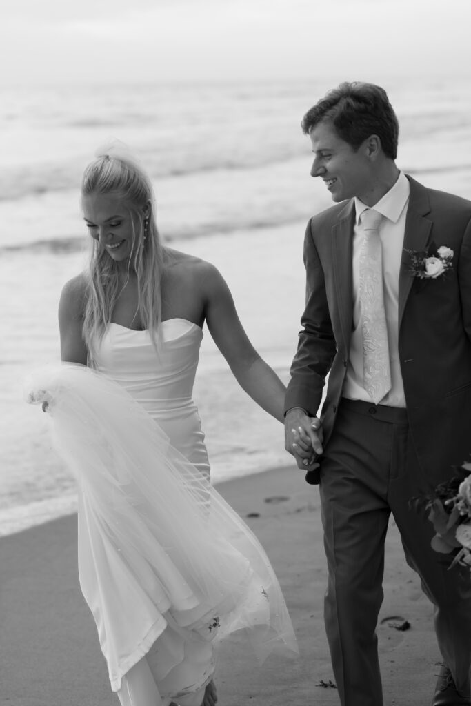 couple holding hands on the beach at their seaside wedding