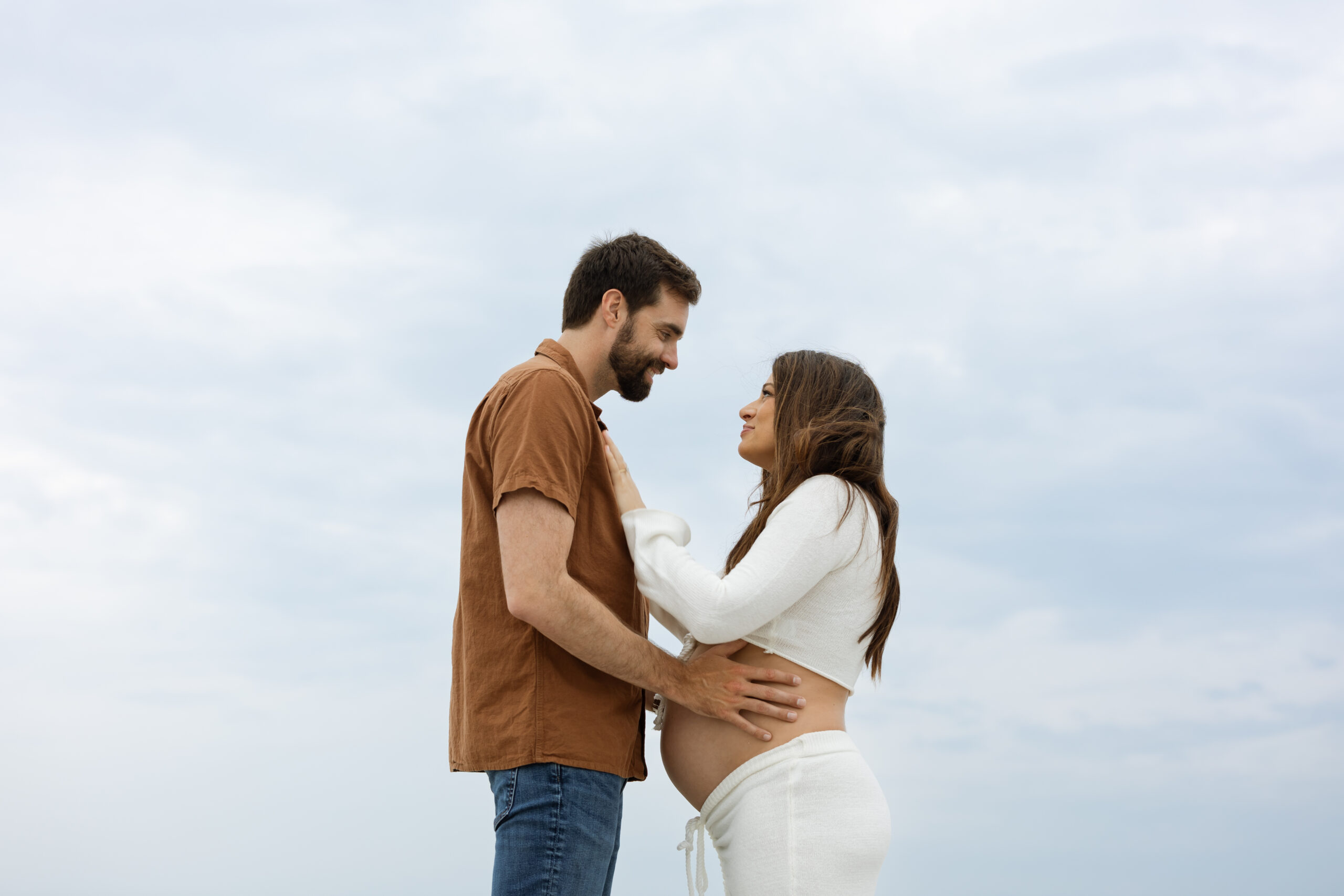 Expecting couple smiling and looking at each other during a Cocoa Beach maternity session at sunset