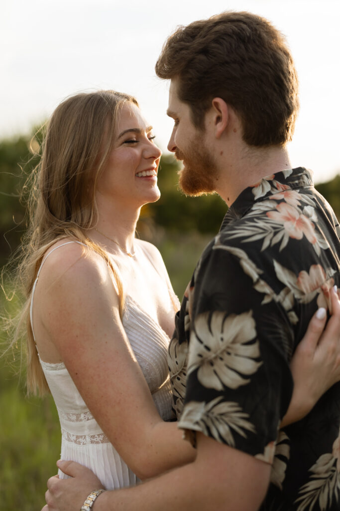Engaged couple laughing together in an open field during a laid-back outdoor engagement session