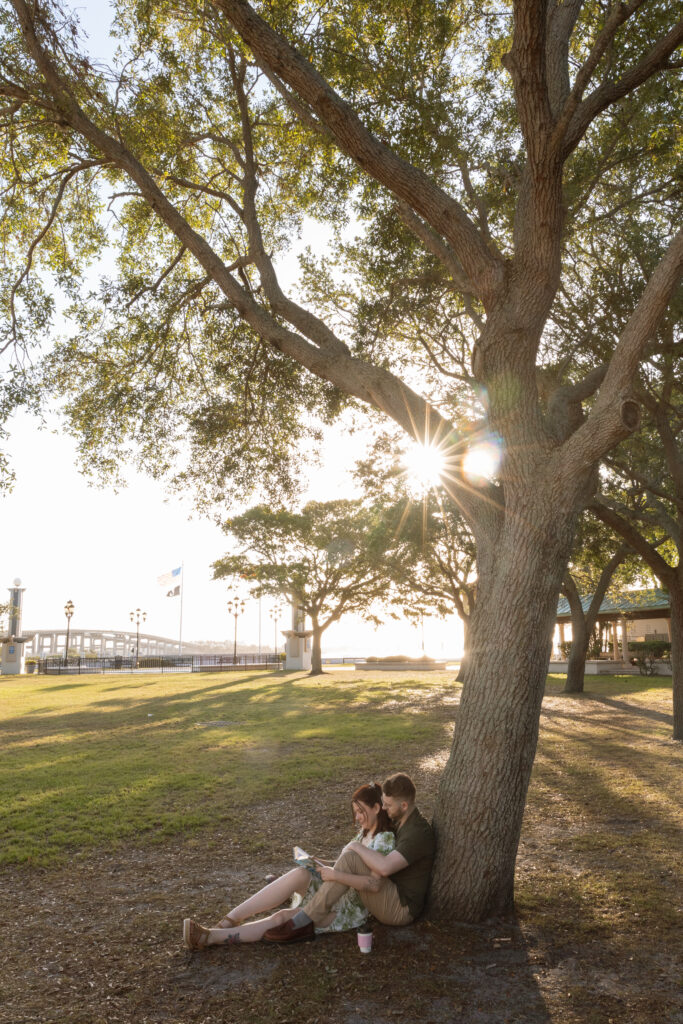 Couple sitting under oak tree in a romantic nature-inspired engagement session